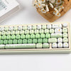 A light green PBT keycap set with MOG profile keycaps and a white case is shown next to a woven basket of white flowers.