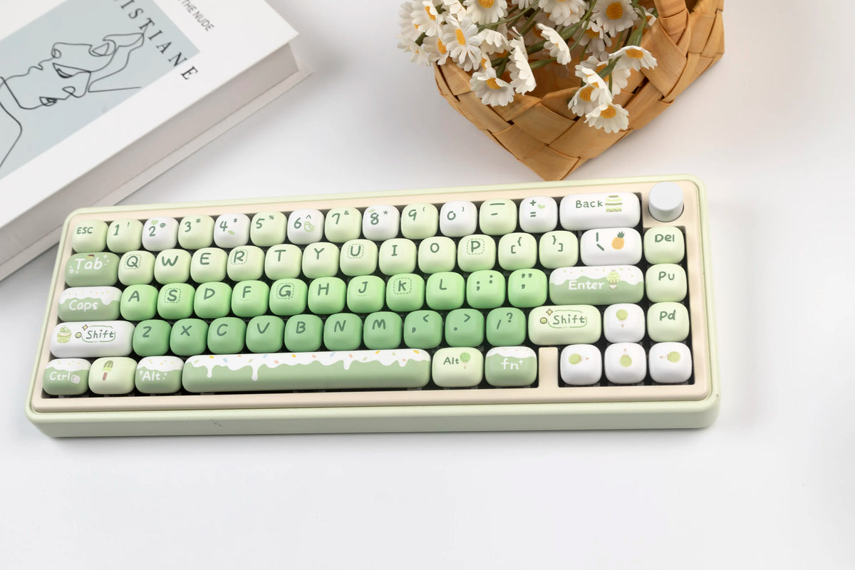 A light green PBT keycap set with MOG profile keycaps and a white case is shown next to a woven basket of white flowers.
