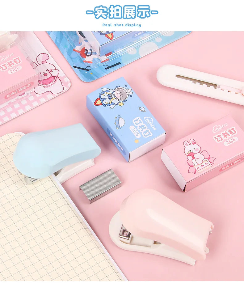 A collection of pink, blue, and white cartoon mini staplers and related stationery items displayed on a light pink background