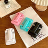 Three adjustable foldable phone and tablet stands in pink, teal, and black resting on a white paper.