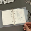 A hand holds open a transparent divider page for loose-leaf planners, showing organized sections and checkmarks.