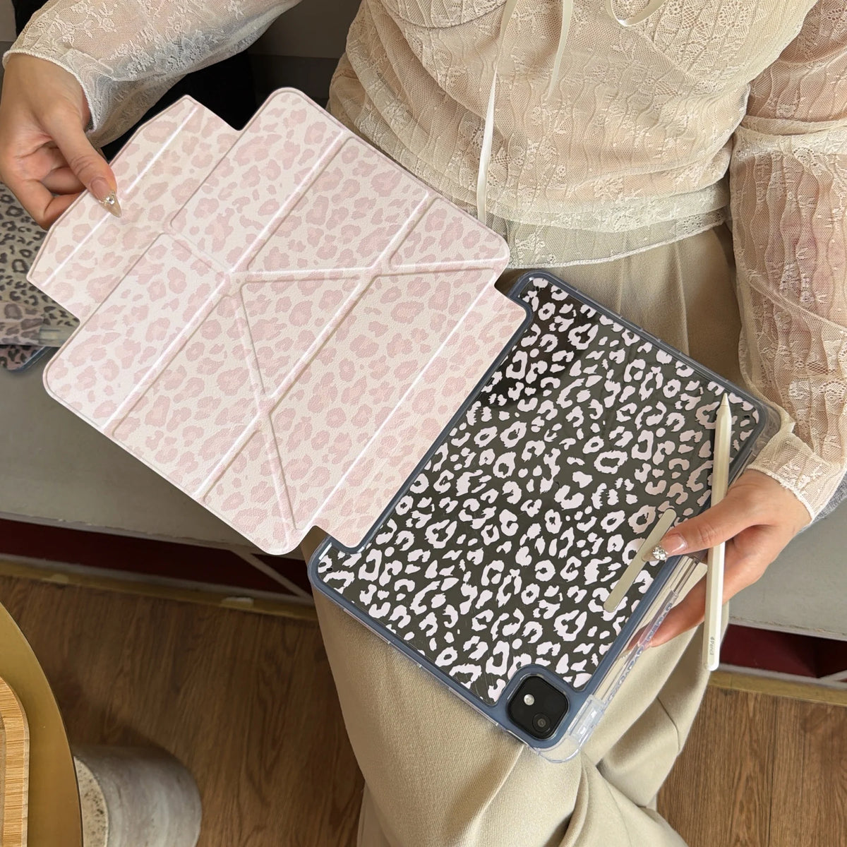 A person holds a pink leopard print leather case for an iPad alongside a dark gray leopard print case.