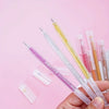 A hand holds a set of 12 glitter gel pens in various vibrant colors against a pink background.
