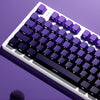A close-up view of a purple mechanical keyboard with gradient keycaps and RGB lighting, resting on a purple surface.