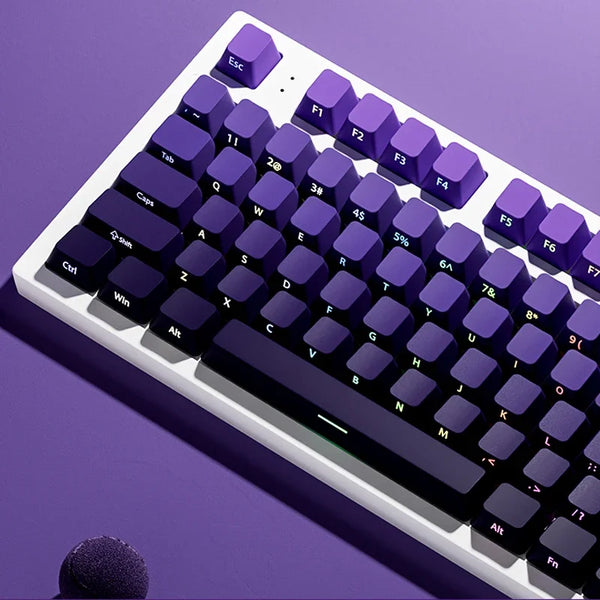 A close-up view of a purple mechanical keyboard with gradient keycaps and RGB lighting, resting on a purple surface.