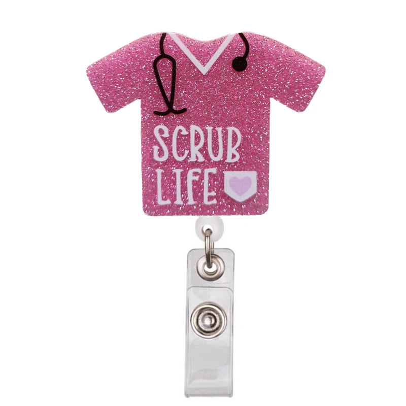 A pink glitter shirt with a black stethoscope design and the text SCRUB LIFE on the front, attached to a badge reel holder.