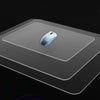 A white wireless mouse resting on a clear frosted glass anti-slip mouse mat.