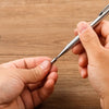 A hand holds a silver precision mechanical pencil, preparing to write or draw.