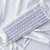 A white mechanical keyboard with custom profile keycaps is shown lying on a white draped fabric.
