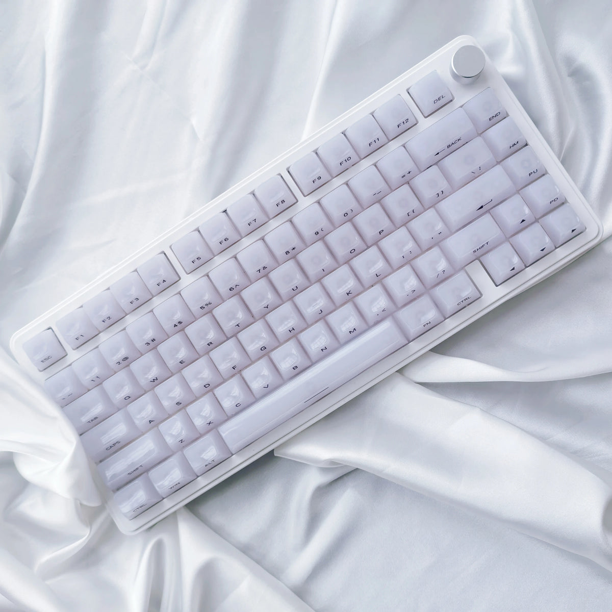 A white mechanical keyboard with custom profile keycaps is shown lying on a white draped fabric.