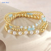 Gold-plated shell pearl beaded bracelets in various shades of blue and white stacked on a light background