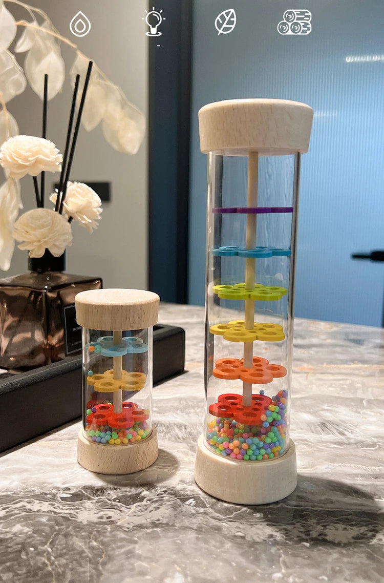 A clear glass tube filled with colorful plastic beads, mounted on a wooden base and held by a wooden top, used as a musical i