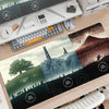 A large gaming mouse pad featuring a Lord of the Rings landscape with mountains and trees on a wooden desk.