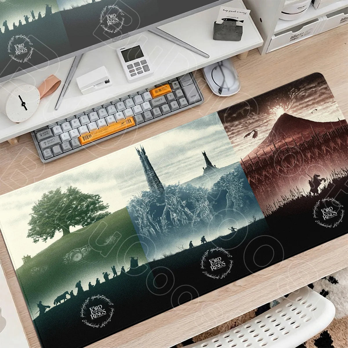 A large gaming mouse pad featuring a Lord of the Rings landscape with mountains and trees on a wooden desk.