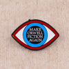 An enamel lapel pin shaped like an eye with the text MAKE ORWELL FICTION AGAIN inside.