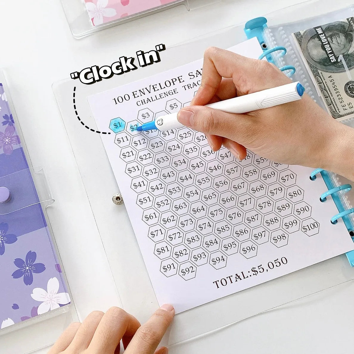 A hand writes on a money saving planner sheet showing numbered envelopes and a total of $5,050