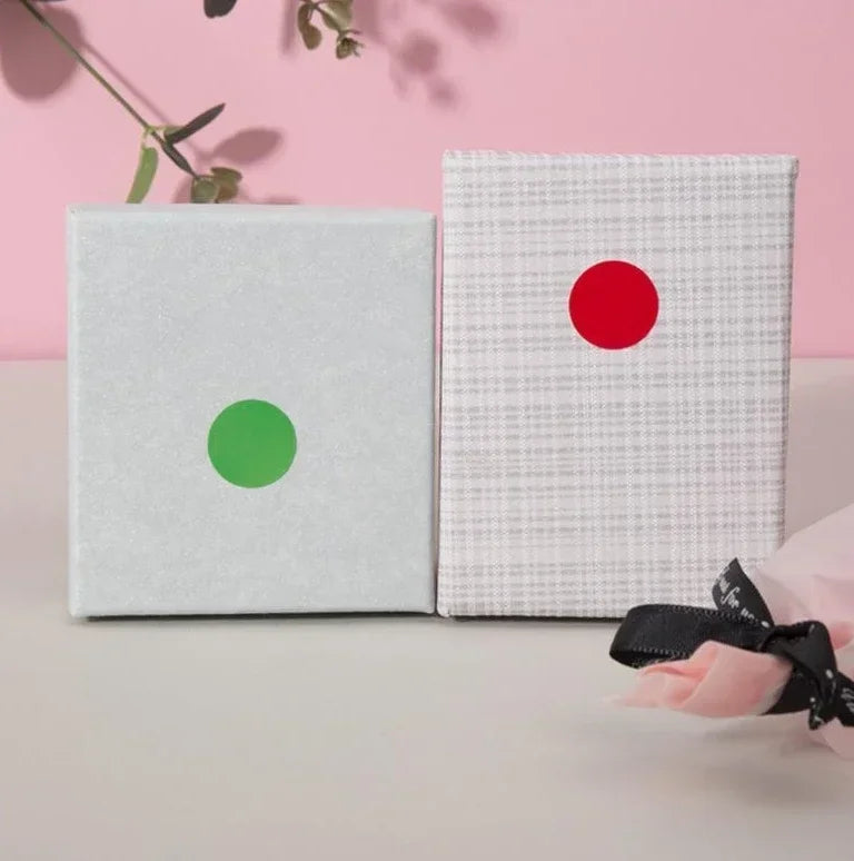 Two square labels, one silver with a green dot and one white with a red dot, are displayed on a light surface.