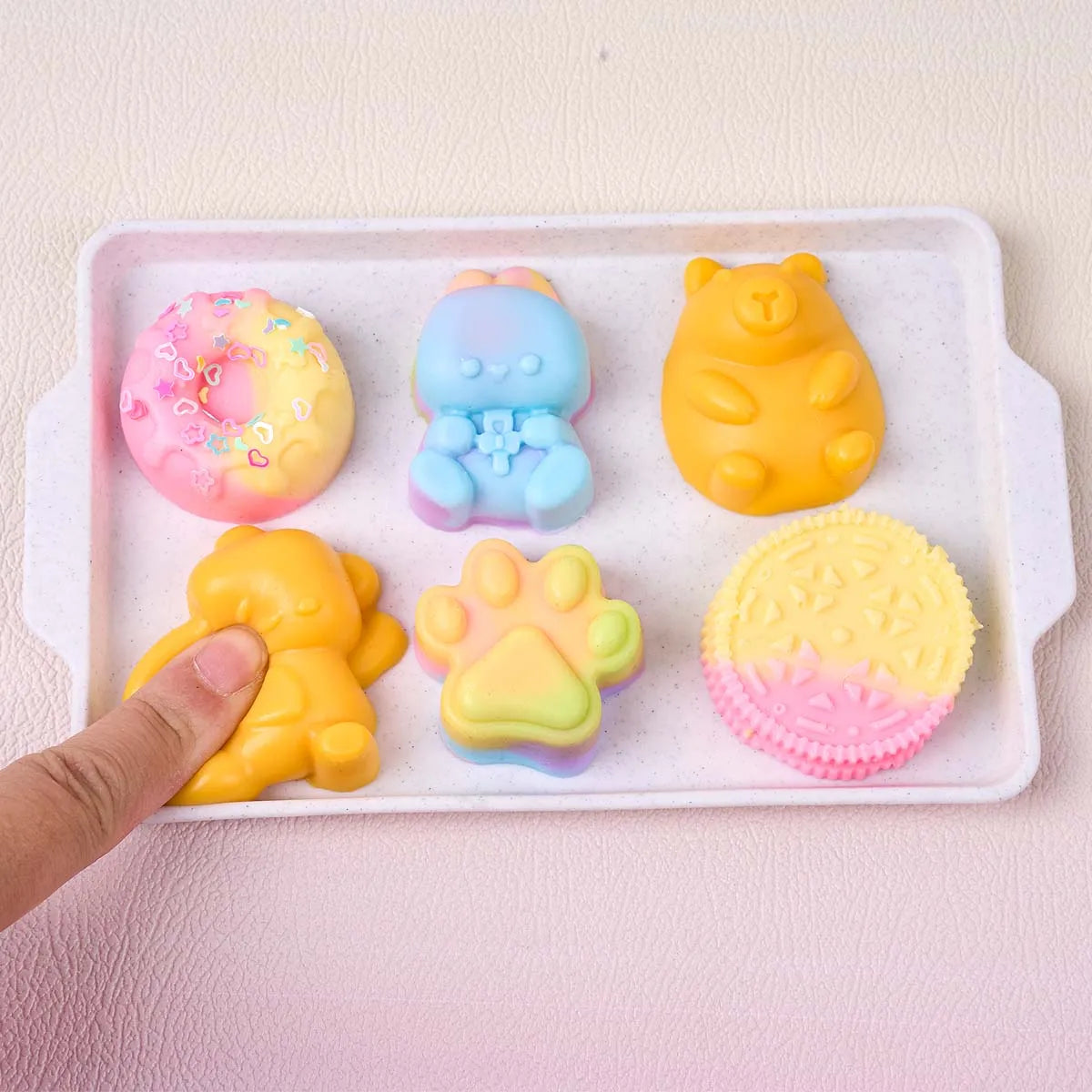 Eine Hand legt verschiedene bunte Silikon-Squishy-Spielzeuge, darunter Teddybären und Pfotenformen, auf eine weiße Schale.