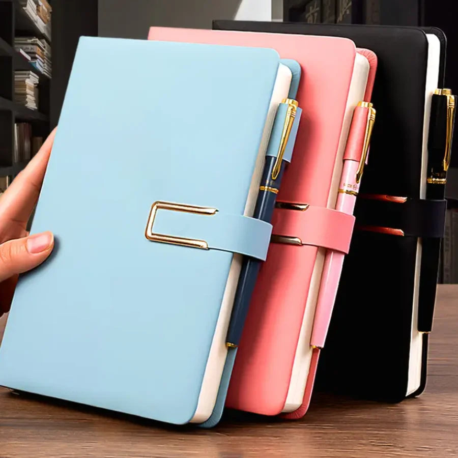 A stack of three A5 retro leather notebooks in light blue, pink, and black with gold accents.