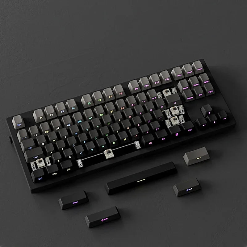 A close-up view of a black mechanical keyboard with gradient gray double shot PBT keycaps and side printing resting on a dark