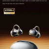 A pair of silver open ear clip Bluetooth earbuds resting on a smooth, light brown surface.