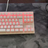 A white mechanical keyboard with pink backlighting and a black gaming mouse resting on a gray mouse pad.