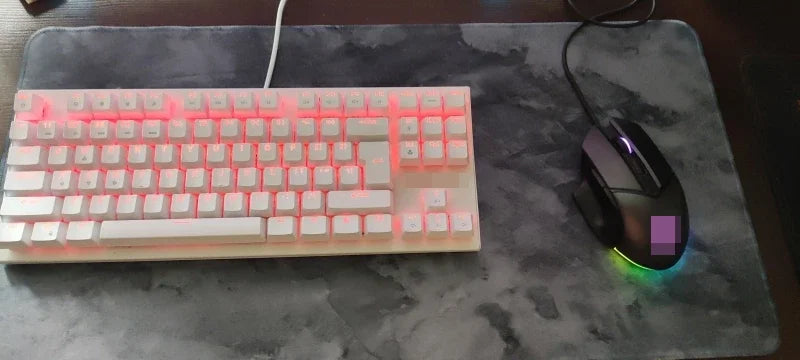 A white mechanical keyboard with pink backlighting and a black gaming mouse resting on a gray mouse pad.