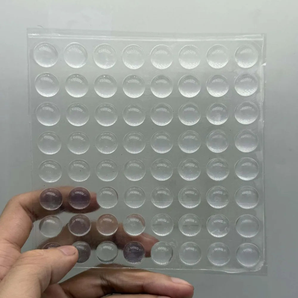 A hand holds a clear silicone sheet with multiple round stickers for long nails on it.