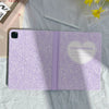 A purple composition book cover with a heart design and a pencil holder lying on a light green cloth.
