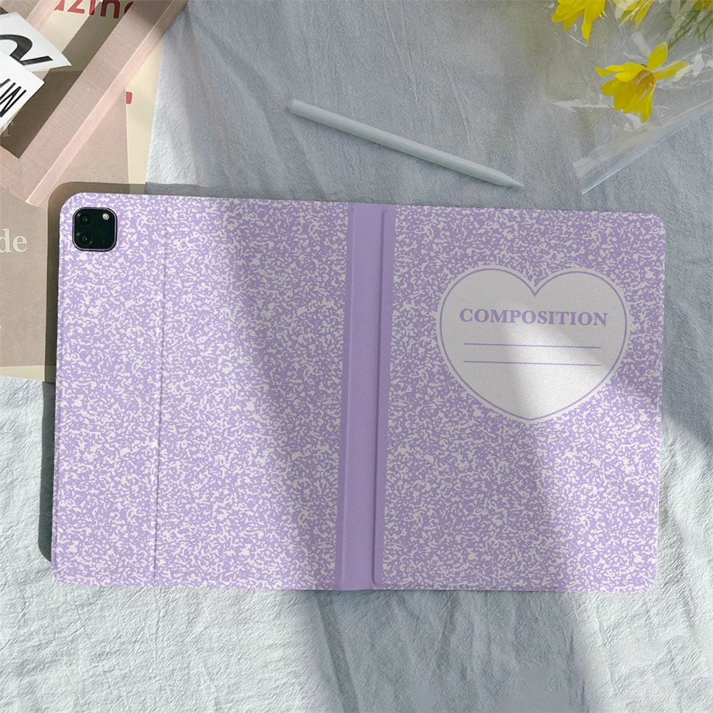 A purple composition book cover with a heart design and a pencil holder lying on a light green cloth.