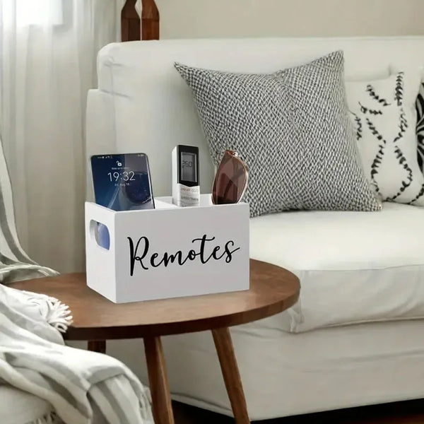 A white wooden storage box with dividers for remote controls is placed on a wooden table next to a white sofa.