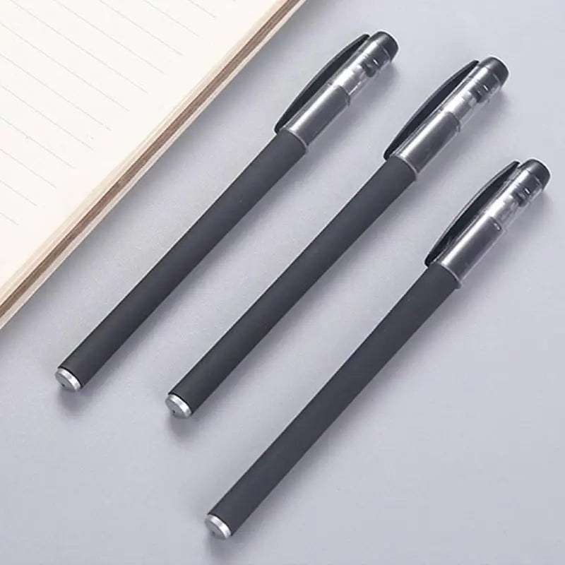 A pack of three black gel ink pens with silver accents lying on a light gray surface.