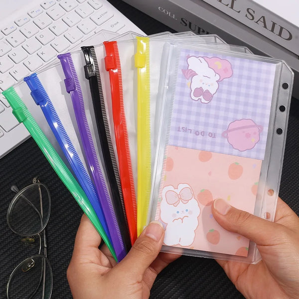 A hand holds a clear PVC zipper binder with colorful pockets for cash and small items.