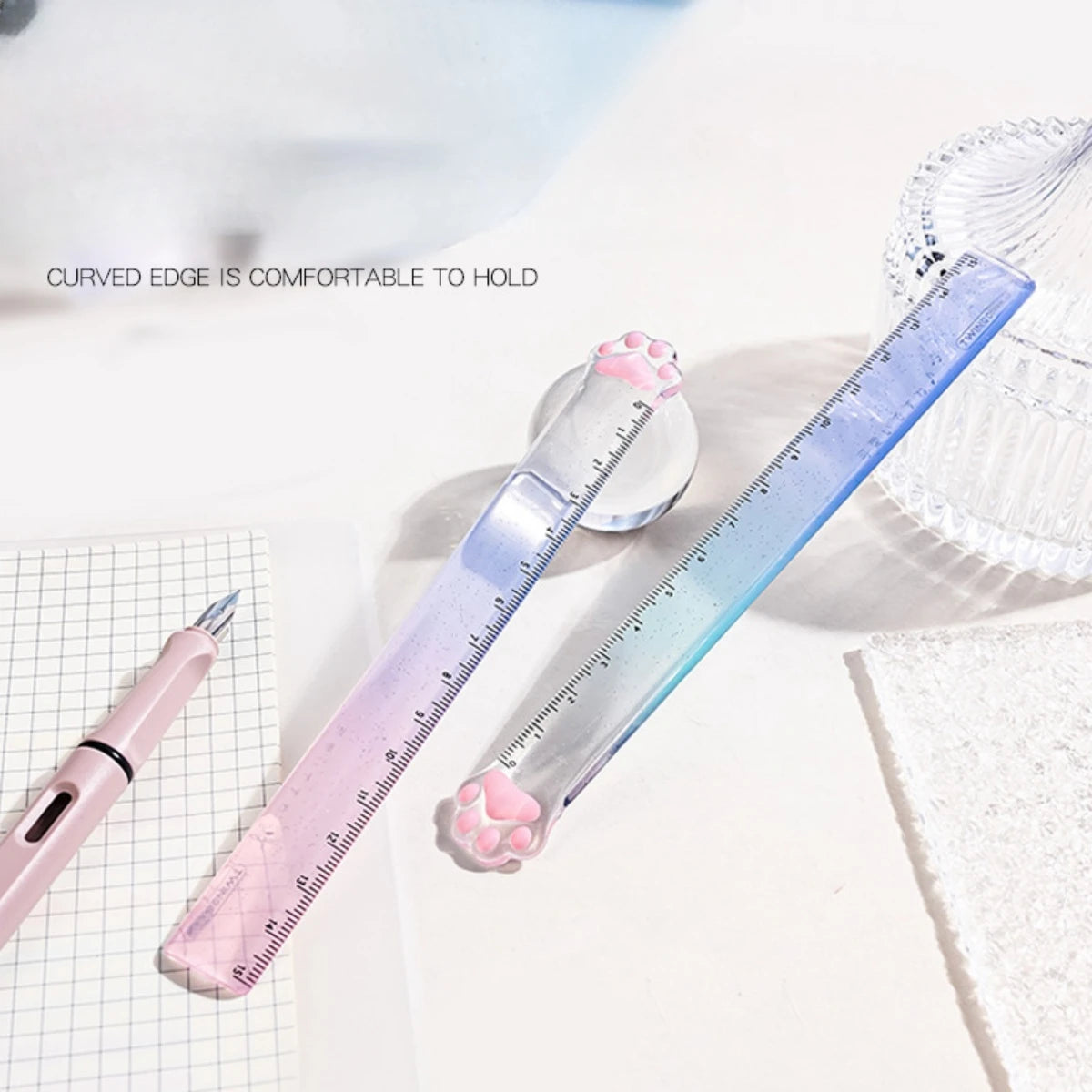 A pink and blue gradient measuring tool with a curved edge is shown next to a ruler and a pencil on a white surface.