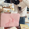 A pink ultra-thin laptop sleeve case is shown resting on a wooden table next to other items.