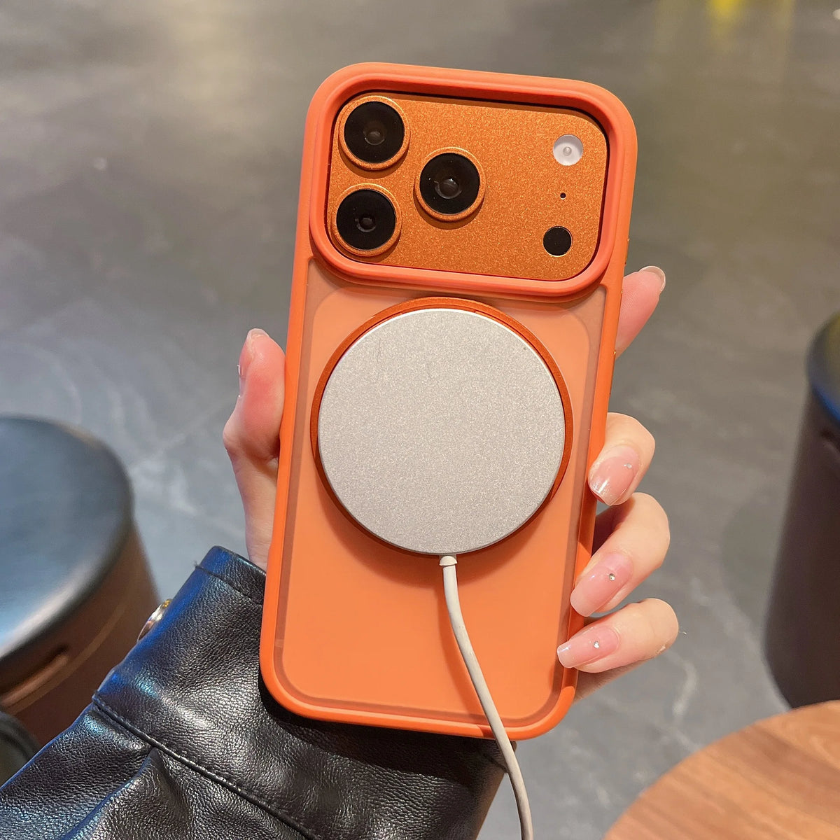 An orange phone case with a magnetic rotating feature and a circular stand is held in a person's hand.