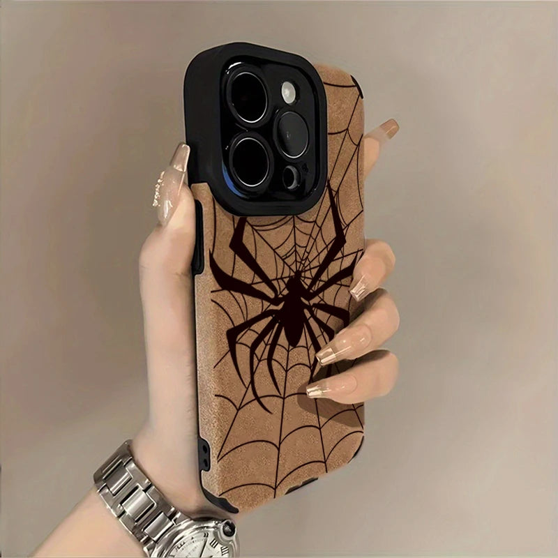 A hand holds a phone case featuring a brown spider web design and a black back, with a silver watch visible.