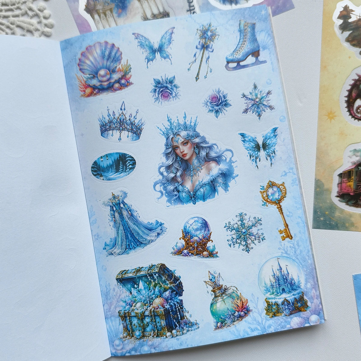A page from a fantasy magic sticker book featuring blue and purple magical elements like fairies, ice crystals, and ornate je