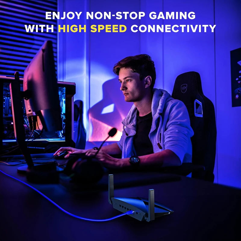 A young man is playing a video game with a computer setup and a blue Ethernet cable connected to the equipment.