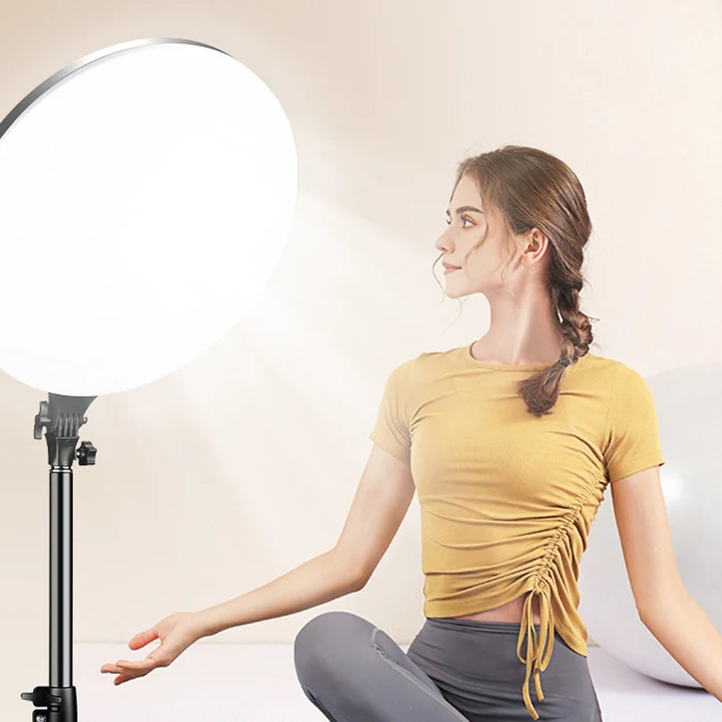 A young woman is using a 10-inch LED ring light with a tripod stand to illuminate her face.