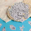 A bundle of white floral embroidery patterns printed on paper rests in a woven basket on a blue surface.