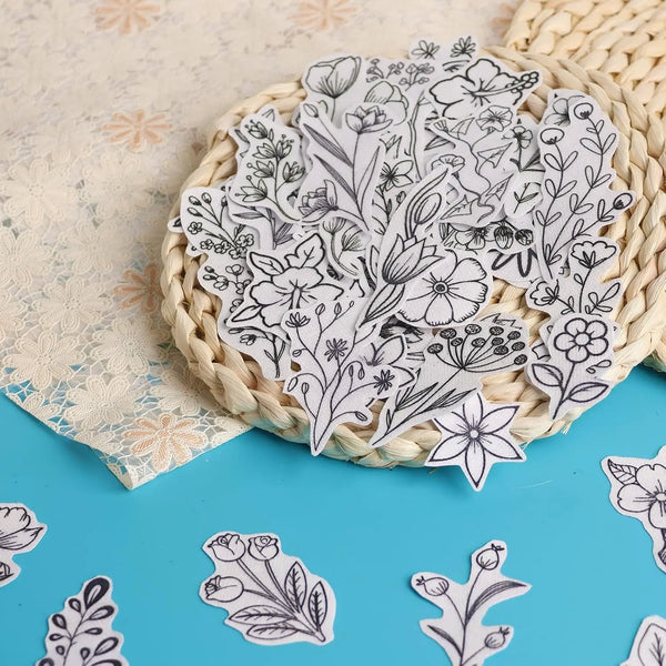 A bundle of white floral embroidery patterns printed on paper rests in a woven basket on a blue surface.