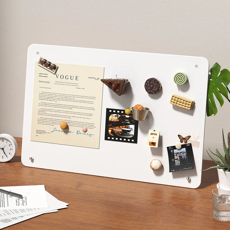 A white magnetic planning board features various items like food samples, notes, and small objects on a wooden desk.