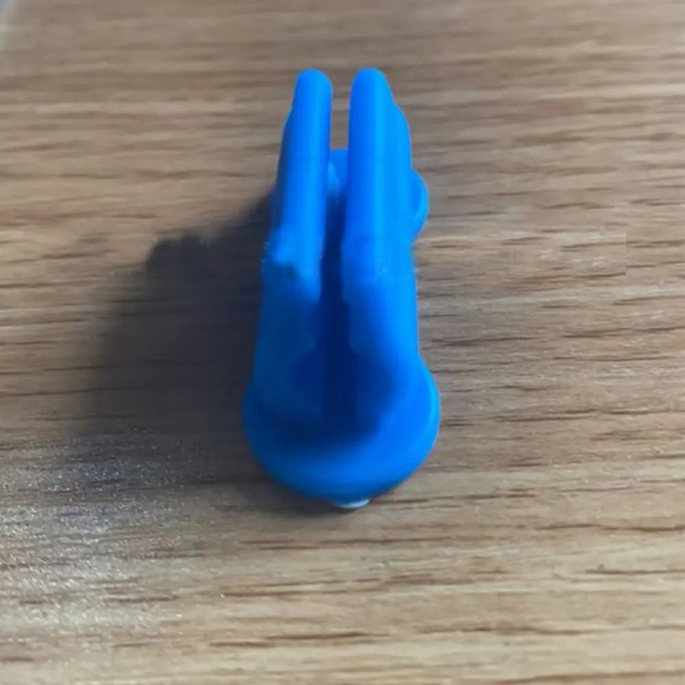 A bright blue silicone self-adhesive pen holder with two prongs resting on a wooden surface.