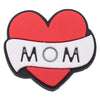A heart-shaped enamel pin featuring the text MOM on a white ribbon against a red background.
