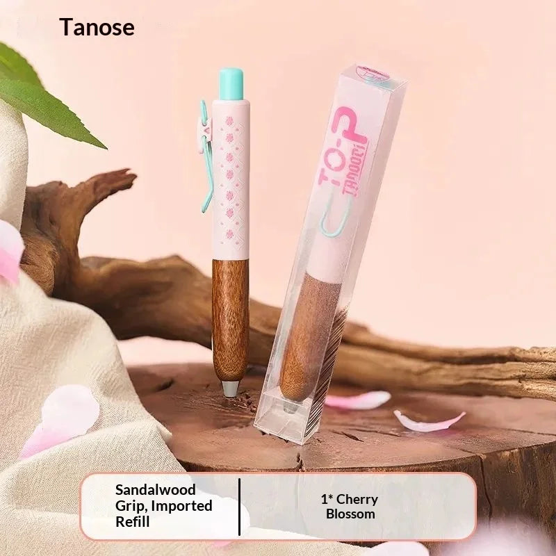Un tubo transparente de bolígrafo gel Tanose con agarre de madera y relleno de flor de cerezo sobre una superficie de madera.