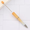 A wooden DIY beadable pen with a silver tip resting on a white tiled surface.