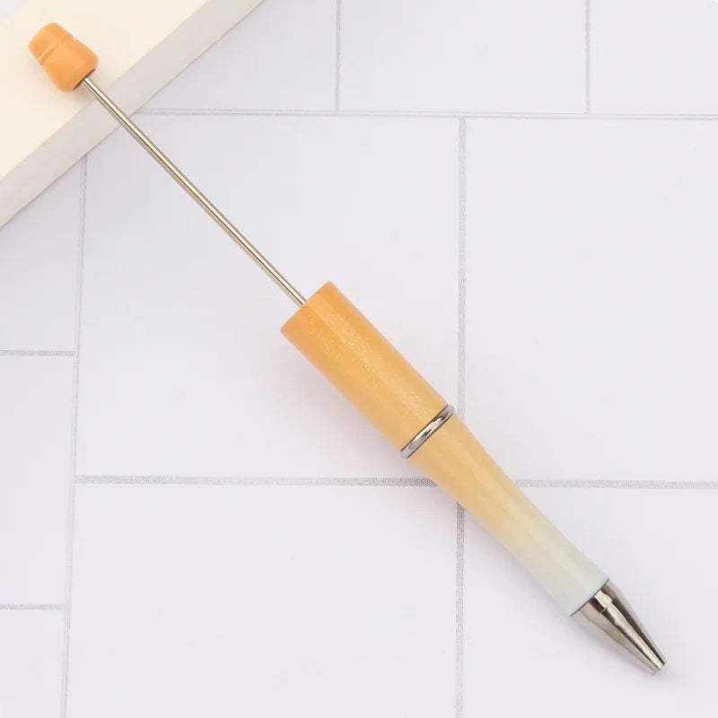 A wooden DIY beadable pen with a silver tip resting on a white tiled surface.
