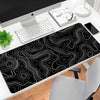A black mouse pad with white contour lines is placed on a desk next to a computer and keyboard.