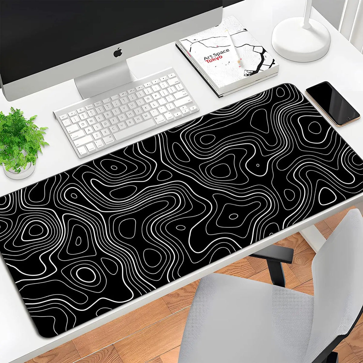 A black mouse pad with white contour lines is placed on a desk next to a computer and keyboard.
